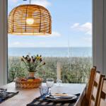 Esszimmer mit Meerblick, Holztisch, Stühle und Wickerlampe.