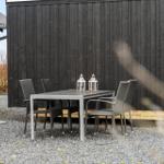 Außenbereich mit Tisch und Stühlen vor dunklem Holzhaus