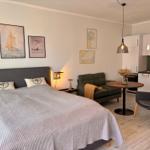 Schlafzimmer mit Bett, Sofa und Küchenbereich. Wandbilder zeigen Segelboote.