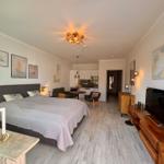 Schlafzimmer mit Bett, Wohnbereich und Küche im Hintergrund.