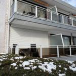 Terrasse mit Tisch und Stühlen, Schnee auf Sträuchern, Balkon mit Glasgeländer