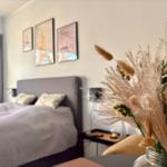 Schlafzimmer mit Bett, Wandbildern und Trockenblumen in Glasflasche.