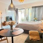 Ein Schlafzimmer mit Bett, Sofa, Tisch und Fernseher. Große Fenster mit Blick auf Balkon.