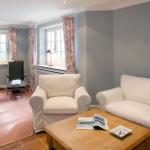 Wohnzimmer mit Sofa, Sessel, Tisch und Fenstern mit Vorhängen.