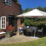 Terrasse mit Tisch, Stühlen und Sonnenschirm vor einem Backsteinhaus mit Blumen.
