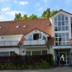 Appartementhaus mit Balkon und rotem Dach unter blauem Himmel.