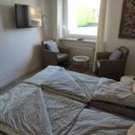 Schlafzimmer mit Bett, zwei Sesseln und Wandfernseher. Fenster mit Blick nach draußen.