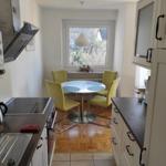 Küche mit Essbereich, runden Tisch und gelben Stühlen. Fenster mit Blick auf Garten.