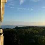 Blick vom Balkon auf Wald und Wasser unter blauem Himmel.