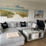 Großer Wohnbereich mit Sofa, Esstisch und Strandmotiven an den Wänden.