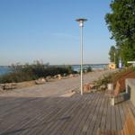 Holzterrasse mit Blick auf Wasser und Bäume. Bank und Laterne sind sichtbar.