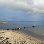 Strand mit Steinen und ruhigem Wasser unter bewölktem Himmel