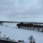 Schneebedecktes Feld mit Bäumen und einer Straße im Vordergrund.