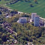 Luftbild von Wohngebieten und Hochhäusern umgeben von grünen Feldern und Bäumen.