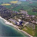 Aerial view of coastal town with beach, hotels, and green fields.