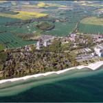 Aerial view of coastal area with beach, green fields, and buildings.