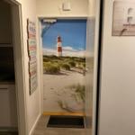 Eingangsbereich mit Leuchtturm-Bild an Tür und Wandtafel mit Regeln.