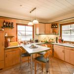 Küche mit Essbereich, Holzschränken und Fenstern mit Jalousien.