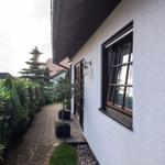 Haus mit gepflasterter Allee, grünen Hecken und Fenstern mit Holzrahmen.