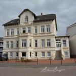 Villa Emilie mit Balkon und Eingangstreppe. Parkplatz und Fahrräder vor dem Haus.