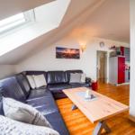 Wohnzimmer mit Sofa, Tisch und Dachfenster. Küche im Hintergrund.