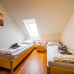 Zwei Einzelbetten, kleiner Nachttisch, Dachschräge mit Dachfenster, Wandbild, Holzboden.