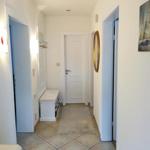 Flur mit weißen Wänden, gefliestem Boden und Tür zu einem Raum