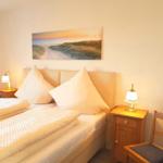 Schlafzimmer mit Bett, zwei Nachttischen und Stühlen. Wandbild zeigt Strand.