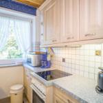 Küche mit Holzschränken, Arbeitsfläche und Fenster mit Vorhängen.