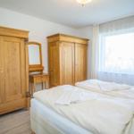 Schlafzimmer mit Holzschrank, Spiegel und Fenster mit Vorhängen.