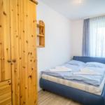 Schlafzimmer mit Holzschrank, Bett und Fenster mit Vorhängen.