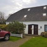 Weiße Villa mit dunklem Dach und zwei Eingangstüren. Vorgarten mit Gras und Strauch.