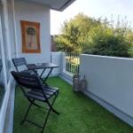 Terrasse mit Tisch, zwei Stühlen und künstlichem Gras. Wandbild und Laternen sind vorhanden.