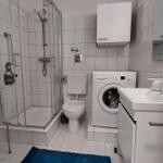 Badezimmer mit Dusche, WC, Waschmaschine und Waschtisch.
