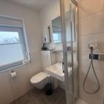 Badezimmer mit Dusche, Waschbecken und Toilette. Fenster mit Blick auf Schnee.