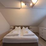 Schlafzimmer mit Doppelbett, Nachttischen und Schrank unter schrägen Dachdecken.