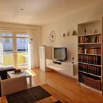 Wohnzimmer mit Sofa, Fernseher und Bücherregal. Durchgang zur Terrasse.