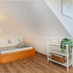 Schlafzimmer mit Dachschräge, Holzbett, Nachttisch und Pflanzen.