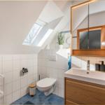Badezimmer mit Dachschräge, Waschbecken, Spiegel und Toilette.