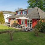 Rotes Haus mit Garten, Terrasse und Sonnenschutz. Grünflächen und Bäume umgeben die Außenanlage.