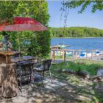 Terrasse mit Tisch, Stühlen und rotem Sonnenschirm am See.