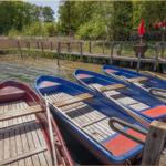 Drei Boote liegen am Bootssteg. Roter und blaue Boote mit Holzplanken.