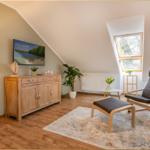 Wohnzimmer mit Sessel, Fernseher und Holzmöbeln unter Dachschrägen.