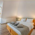 Schlafzimmer mit Dachschrägen, Holzbett, Nachttisch und Fenster mit Blick auf Bäume.