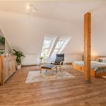 Schlafzimmer mit Dachschrägen, Bett, Sessel und Holzboden.