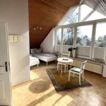 Zimmer mit Dachschrägen, Fenster und Holzboden. Tisch, Stühle und Bett sind vorhanden.