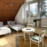 Zimmer mit zwei Betten, Tisch und Stühlen, großem Fenster und Holzdecke.