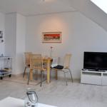 Wohn- und Essbereich mit TV, Tisch und Stühlen unter schrägem Dach