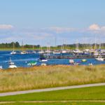 Ein Fahrrad fährt entlang eines Grasstreifens zum Hafen mit vielen Booten.