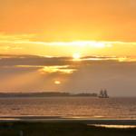 Sonnenuntergang über dem Meer mit Segelschiff und Strand im Vordergrund.